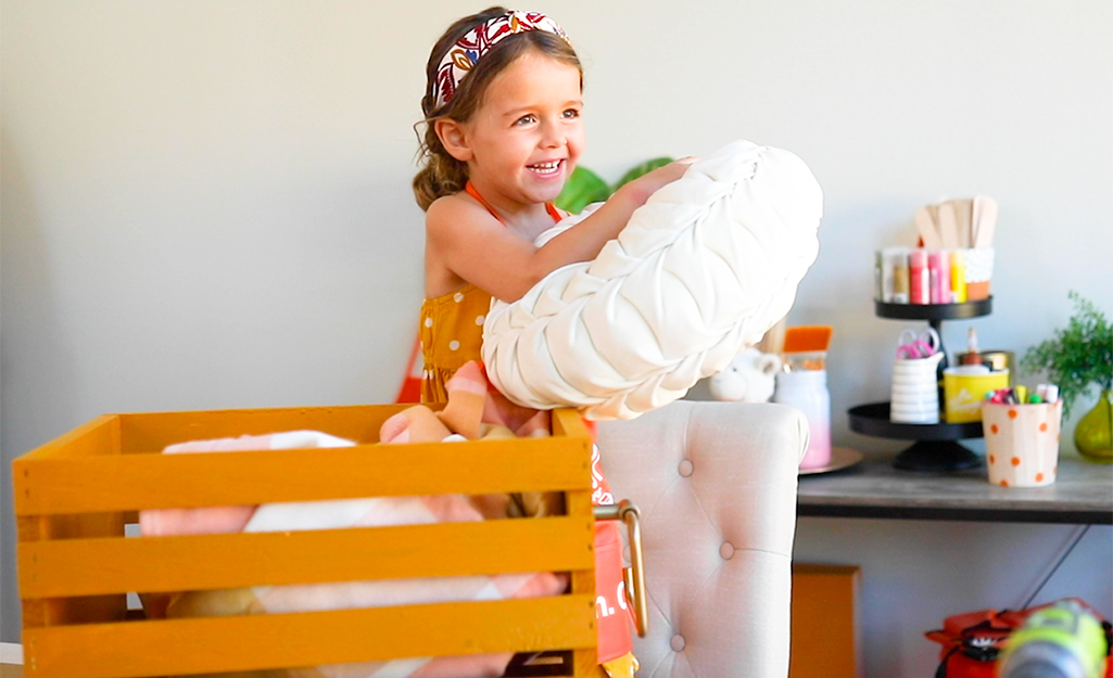 A little girl adds pillows and blankets into a painted crate.