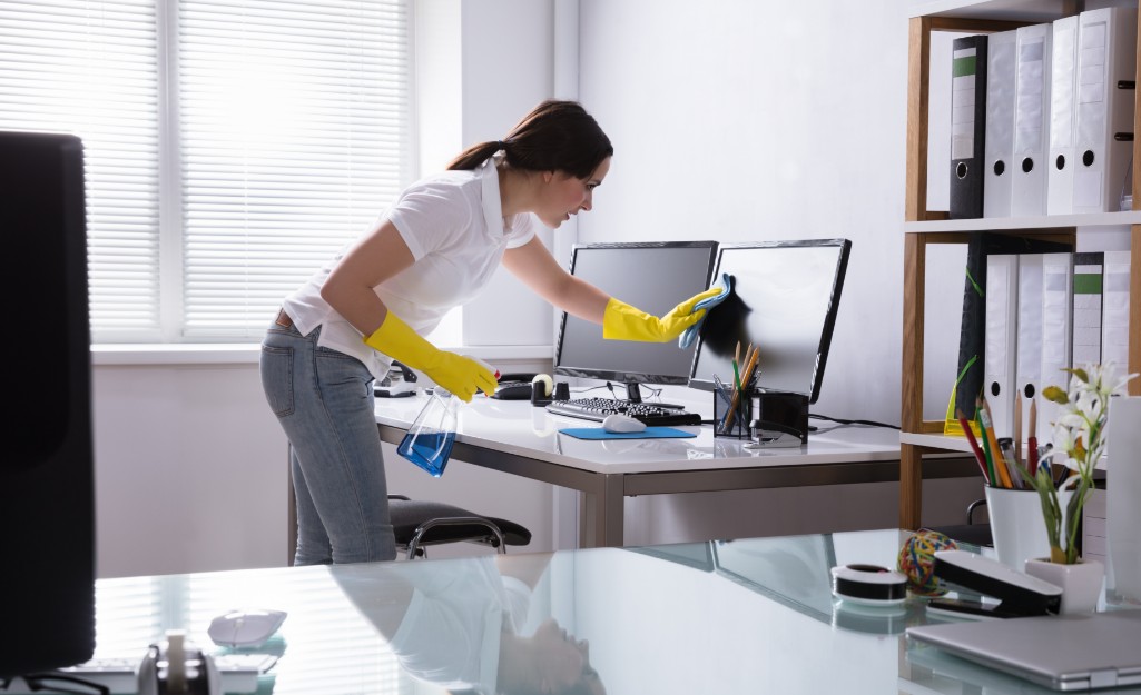 A worker cleans a desk and computer monitor
