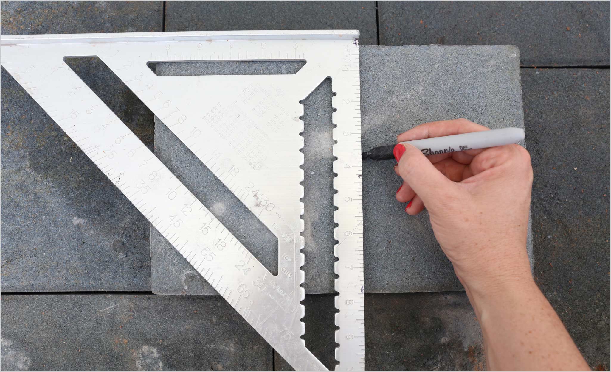 A Pro marks a paver cutline with a Sharpie and a drafting triangle.