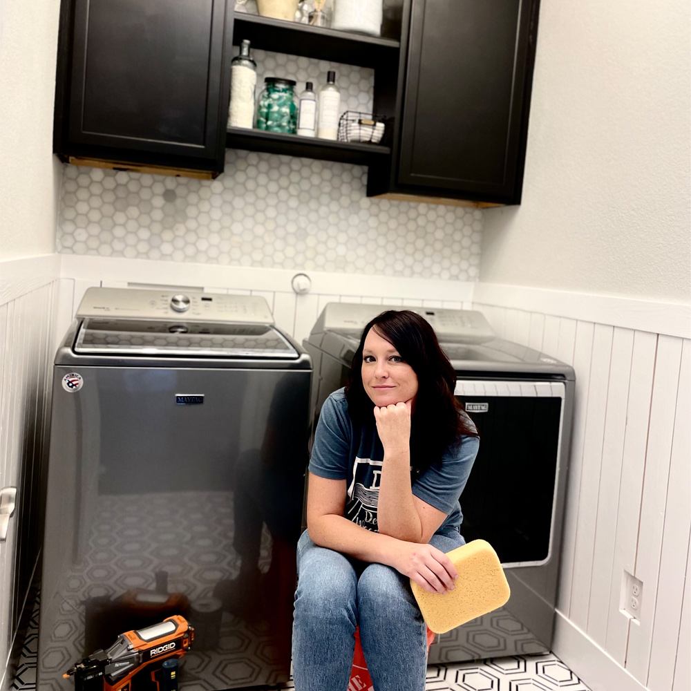 Woman sitting in the laundry room in front of the washing machine and dryer.