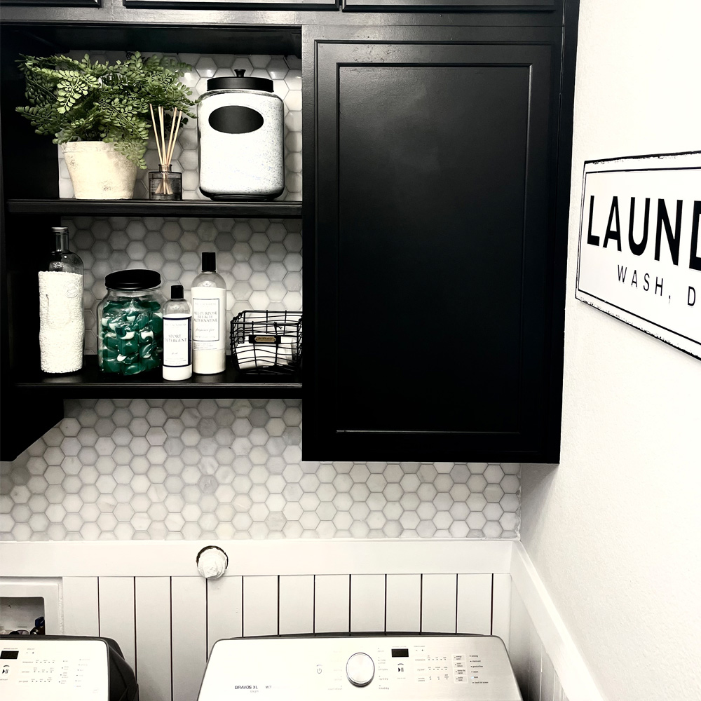 Close up of laundry room cabinets with decorated shelves, a sign, and wall tiling.