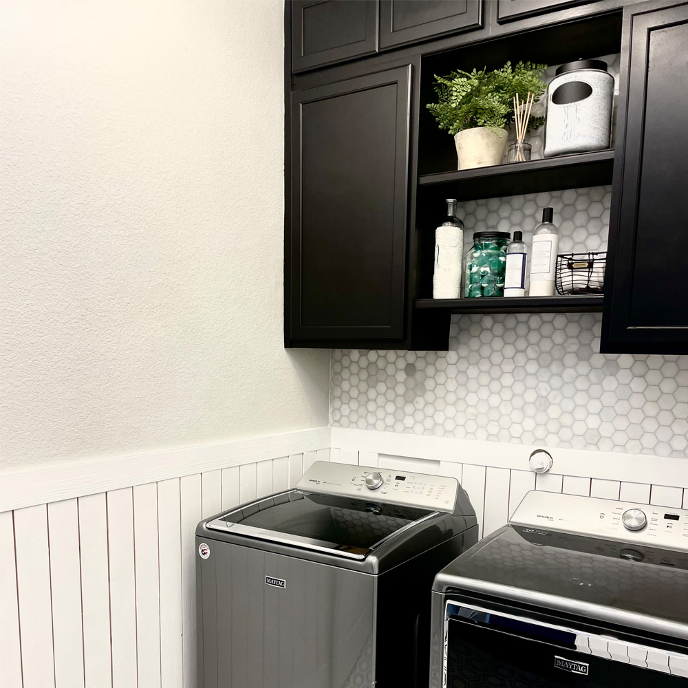 Laundry room with decorated cabinet, wall tiling, washing machine, and dryer.