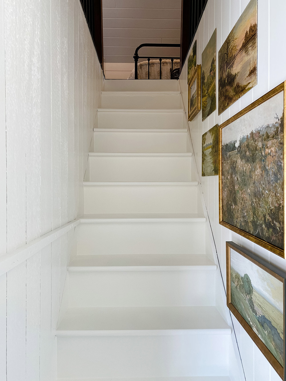 Freshly painted white staircase with framed paintings on right wall.