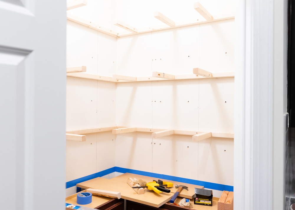A Pantry corner lined with wooden panels and blue scotch tape with tools sitting on a wooden counter top 