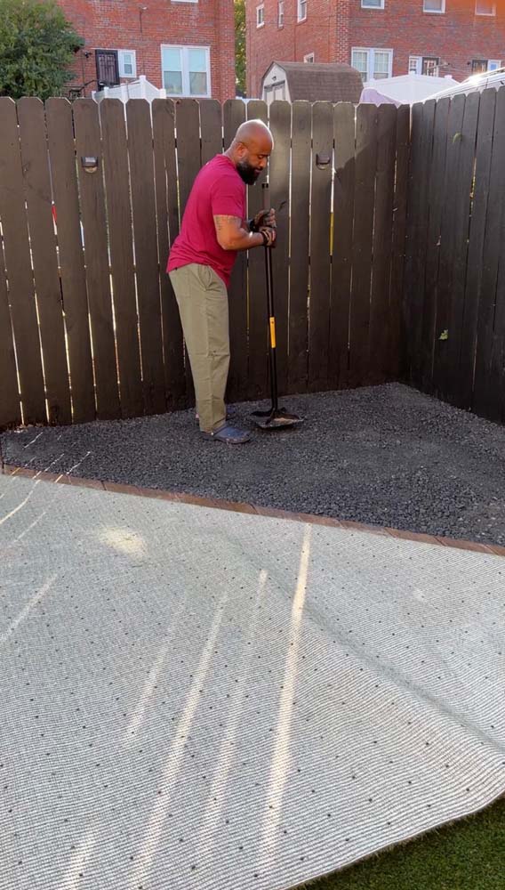 Man in red shirt standing on grey gravel corner with hand tamp stamping down gravel