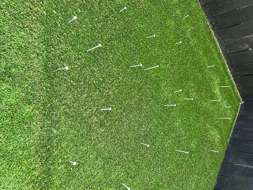Corner of outdoor patio covered in green grass turf with nails dispersed evenly throughout turf 