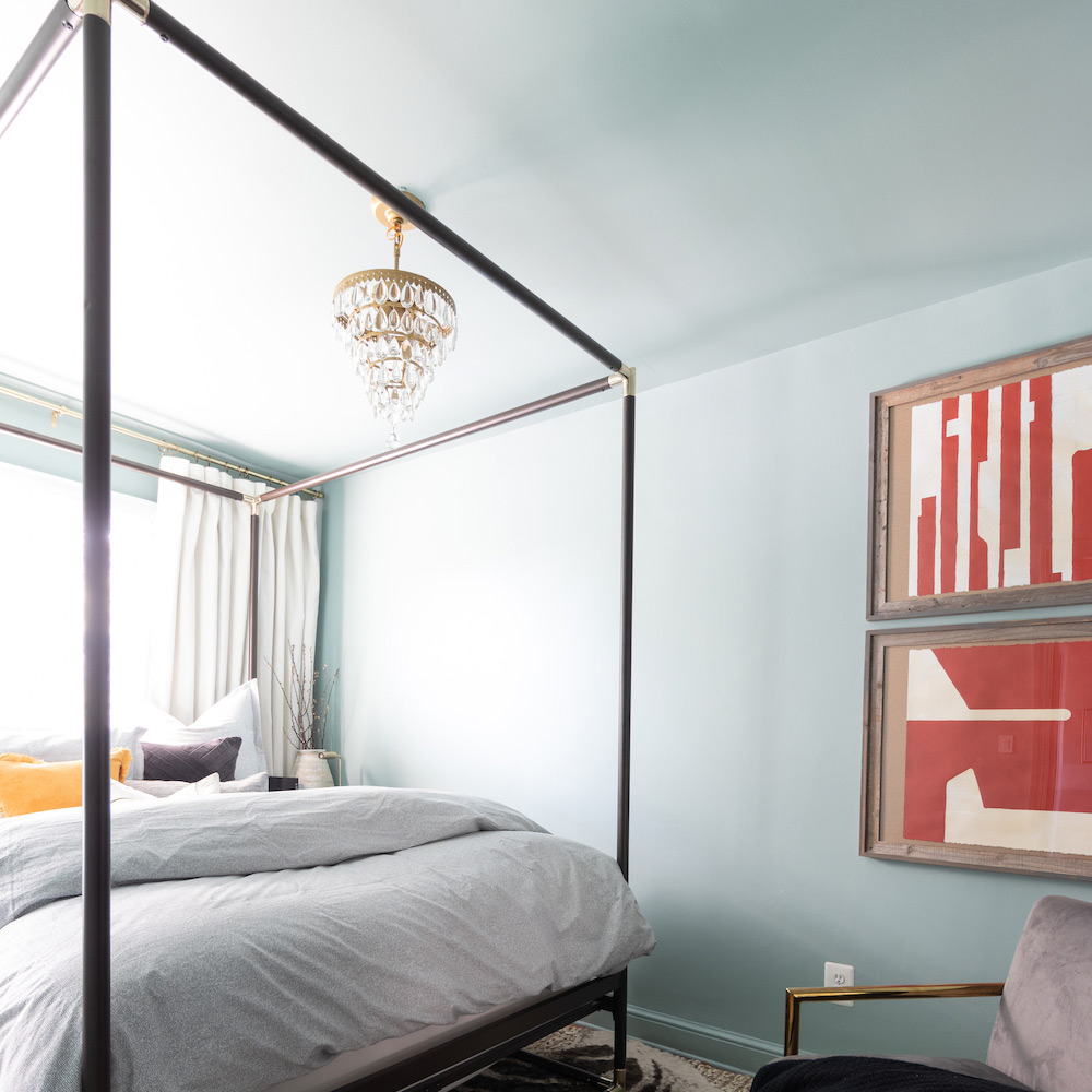 A bedroom with light blue walls, a canopy bed, and artwork on the walls. A bedroom with light blue walls, a canopy bed, and artwork on the walls.