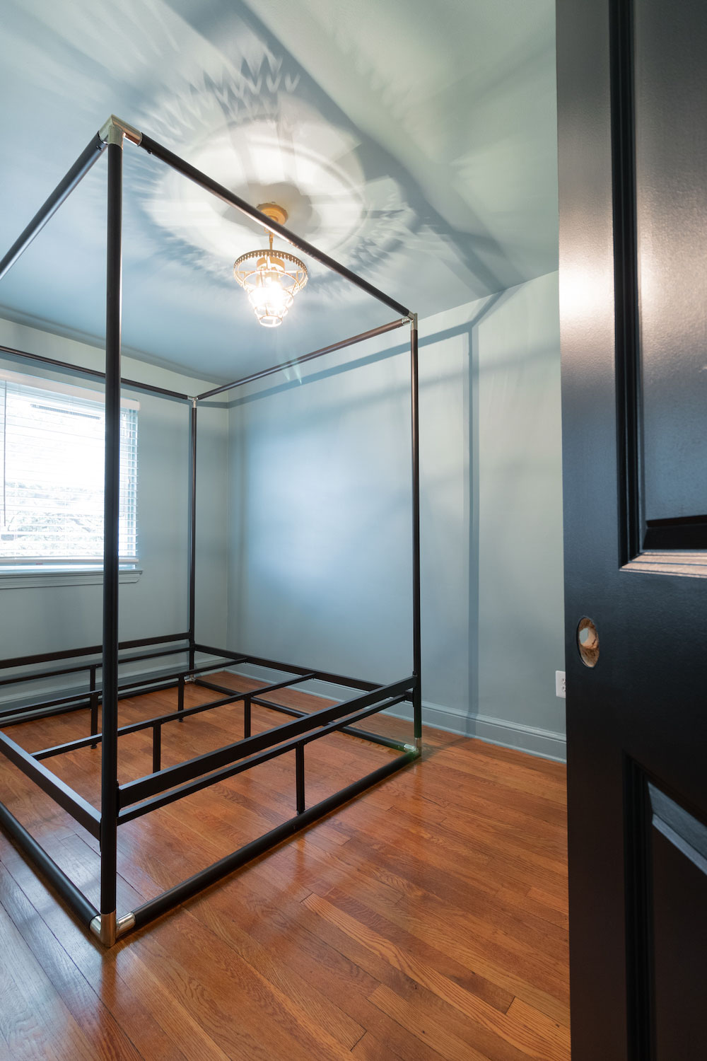 A large black canopy bed frame sitting in an undecorated bedroom. A large black canopy bed frame sitting in an undecorated bedroom.