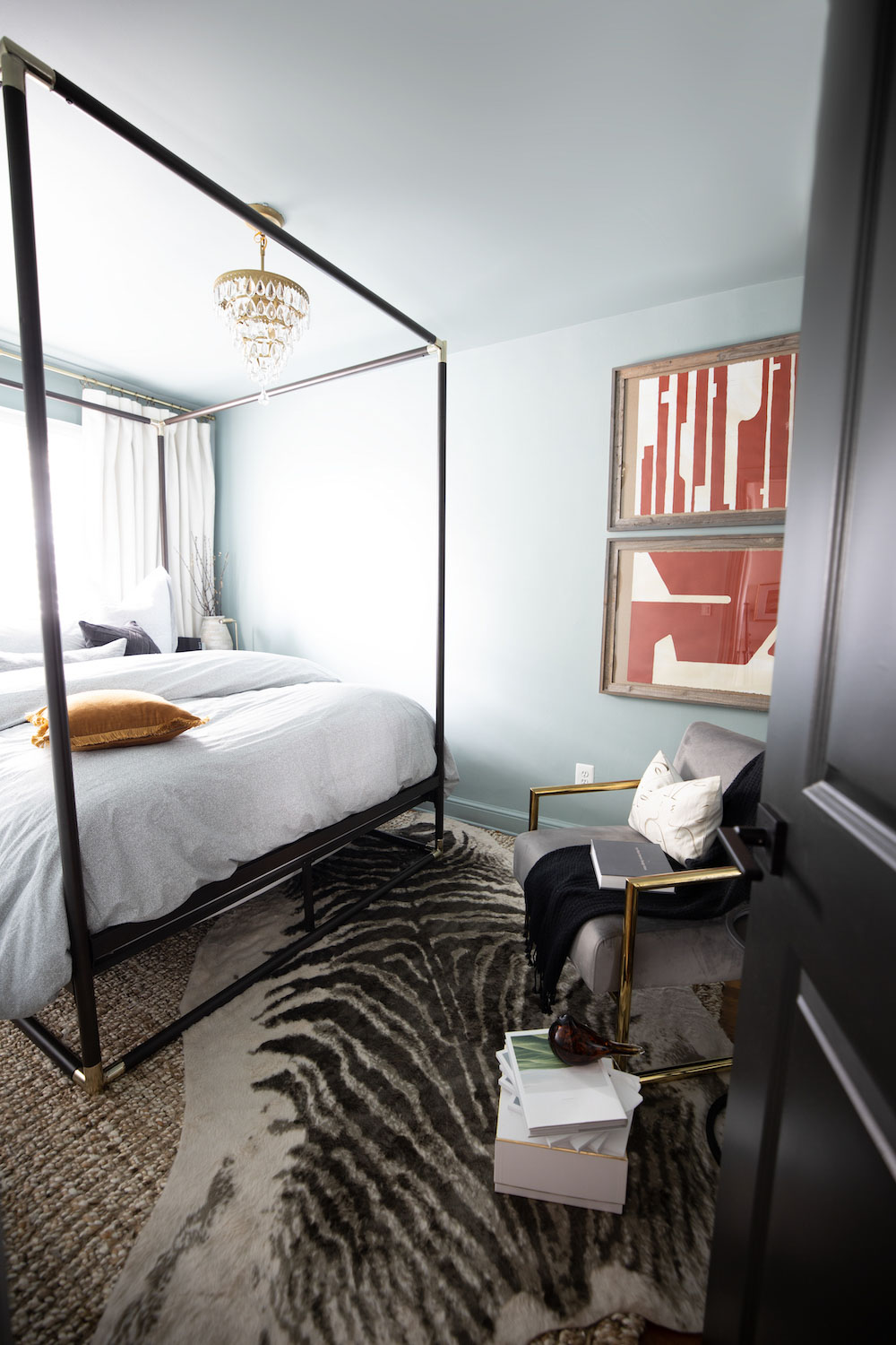 A bedroom decorated with a zebra rug, black canopy bed, and a gray velvet accent chair. A bedroom decorated with a zebra rug, black canopy bed, and a gray velvet accent chair.