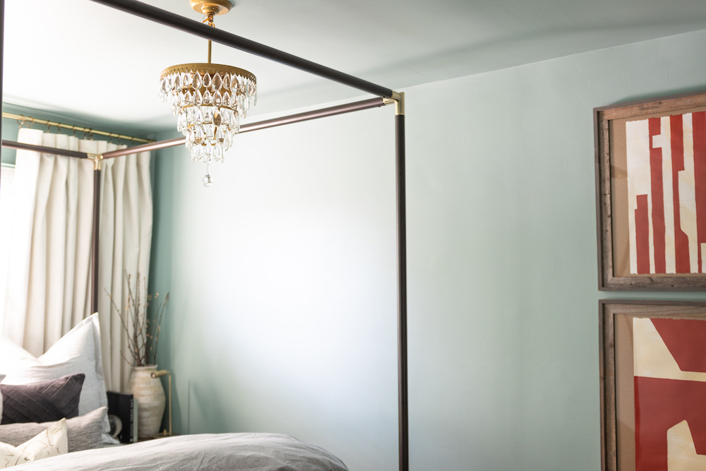A brass and glass tear drop chandelier hangs above a black canopy bed. A brass and glass tear drop chandelier hangs above a black canopy bed.
