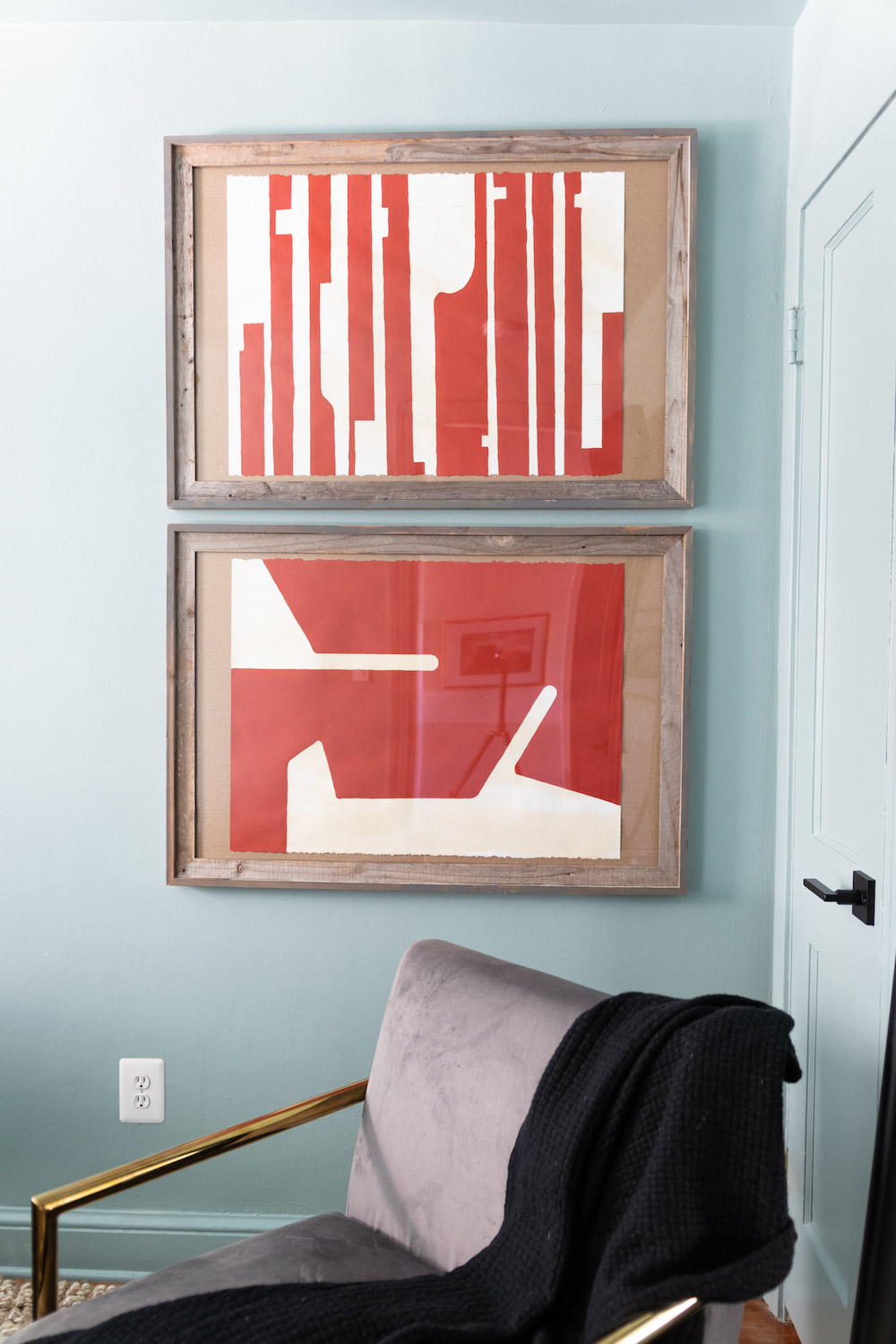 A light blue wall decorated with red abstract art in large distressed frames. A light blue wall decorated with red abstract art in large distressed frames.