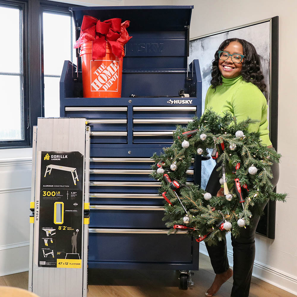 A woman holding a wreath decorated with tools in front of a tool chest.