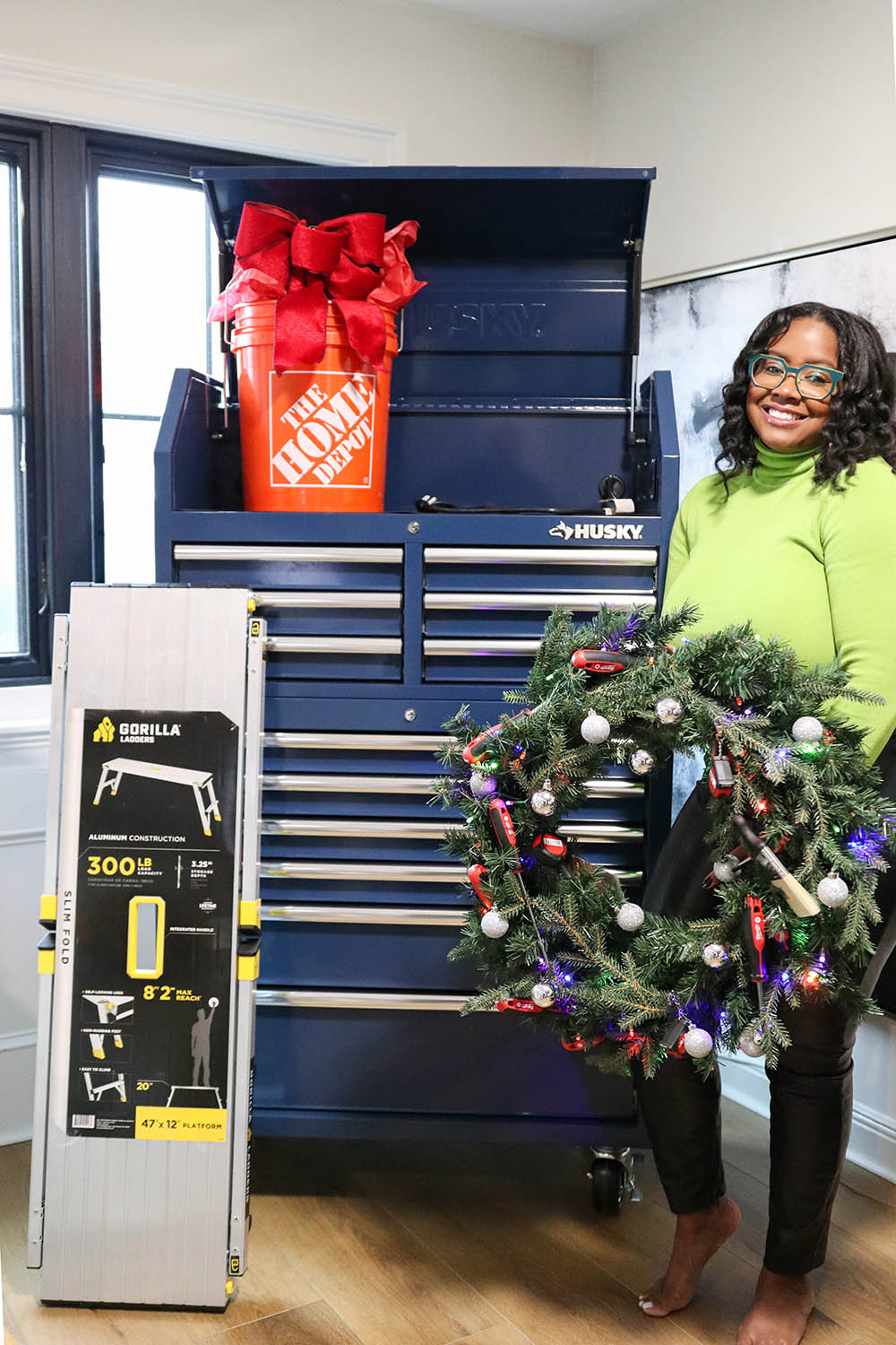 A woman holding a wreath decorated with tools in front of a tool chest.