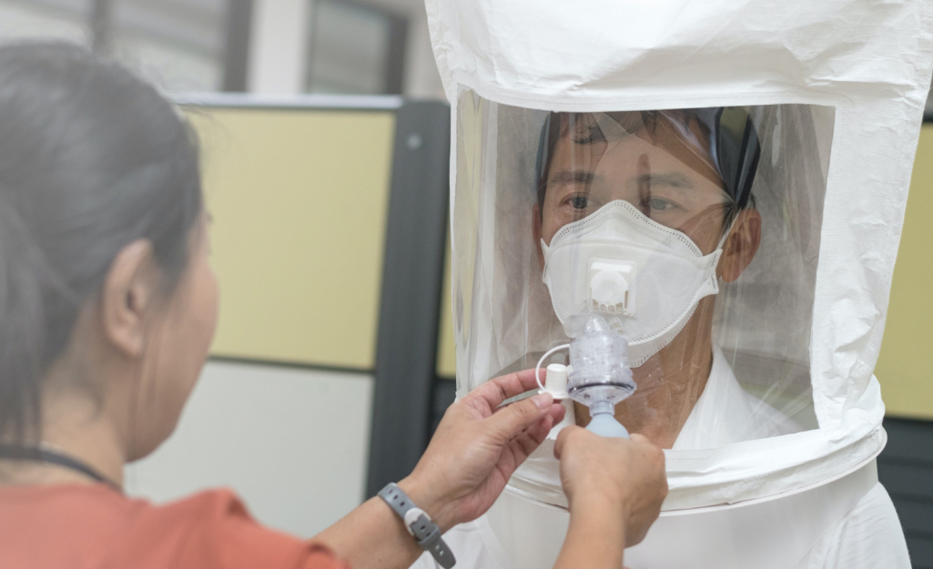 A worker wears a test hood over a respirator.
