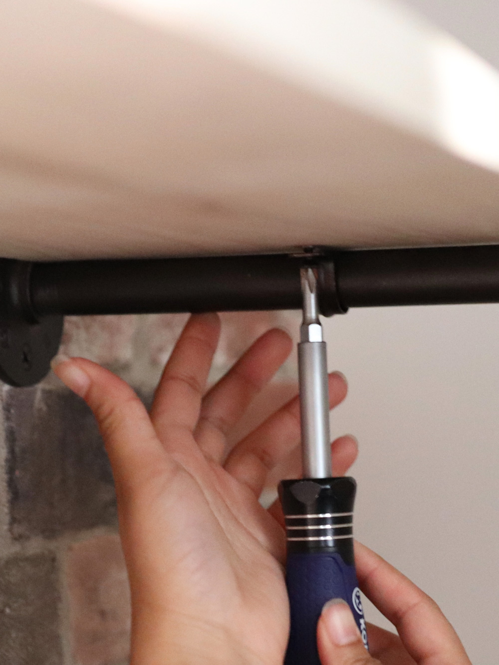 A person secures a board and pipe together using a screwdriver and wood screw. A person secures a board and pipe together using a screwdriver and wood screw.