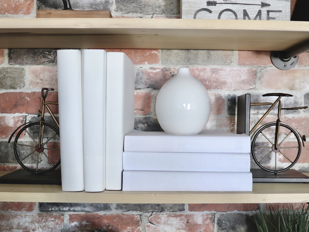A bookshelf decorated with white books and brass-finished bicycle bookends. A bookshelf decorated with white books and brass-finished bicycle bookends.