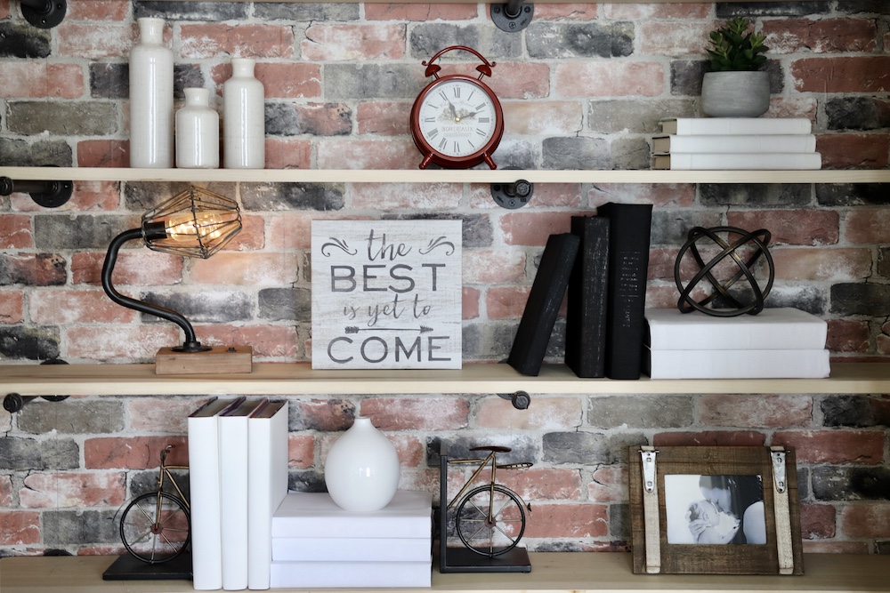 A group of decorated bookshelves in front of a wall with brick wallpaper. A group of decorated bookshelves in front of a wall with brick wallpaper.