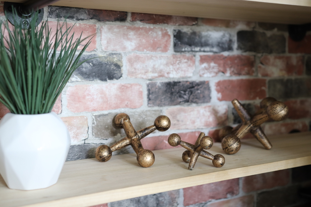 A set of brass finished decorative jacks sit on a wooden bookshelf.