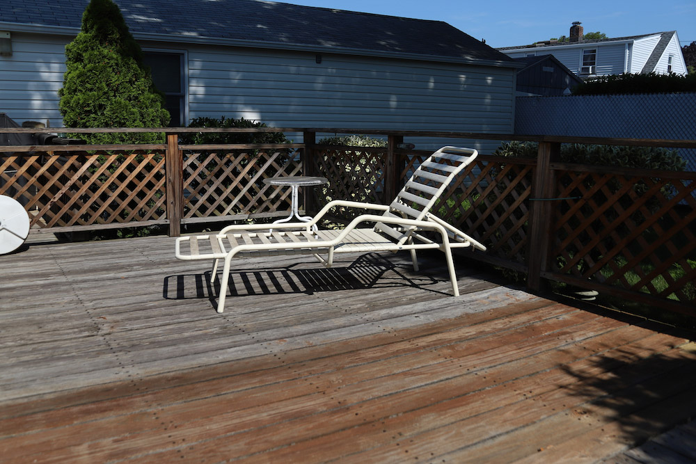 An old white patio chair sits on an unstained deck. An old white patio chair sits on an unstained deck.