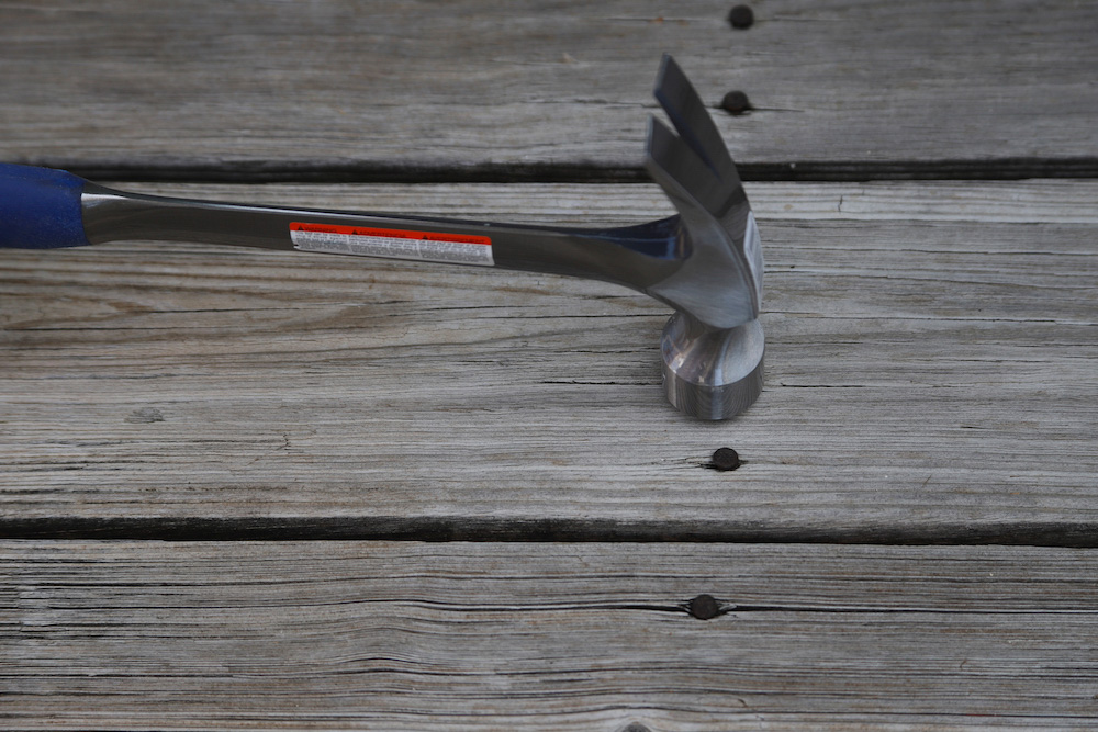 A hammer taps a nail in a deck board. A hammer taps a nail in a deck board.