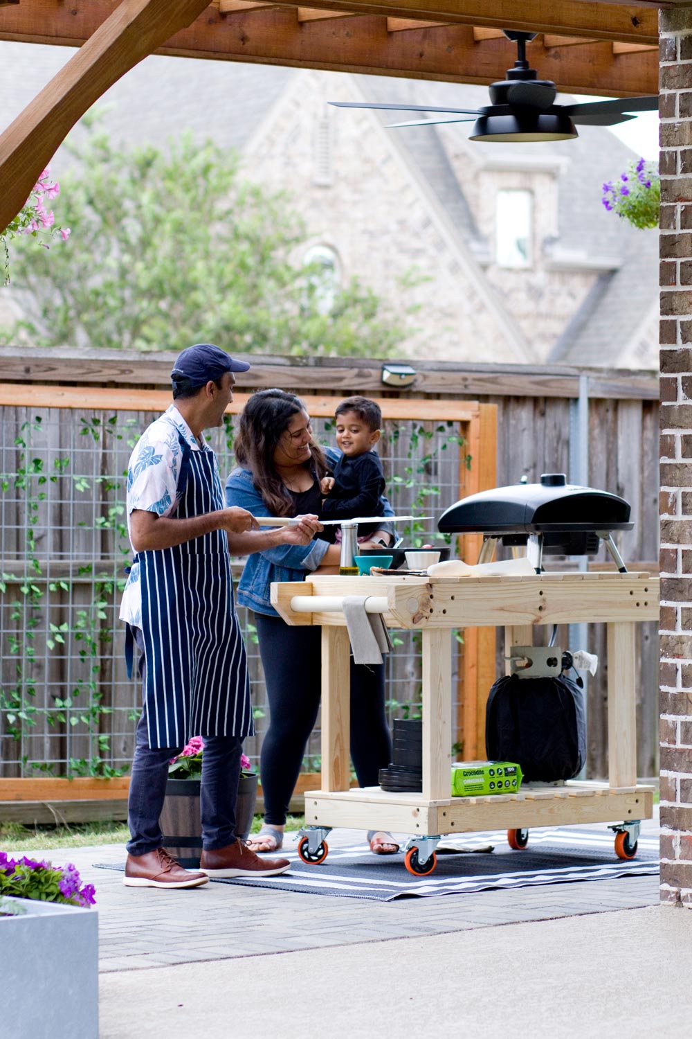A man, and woman holding a child standing behind a wooden rolling cart.
