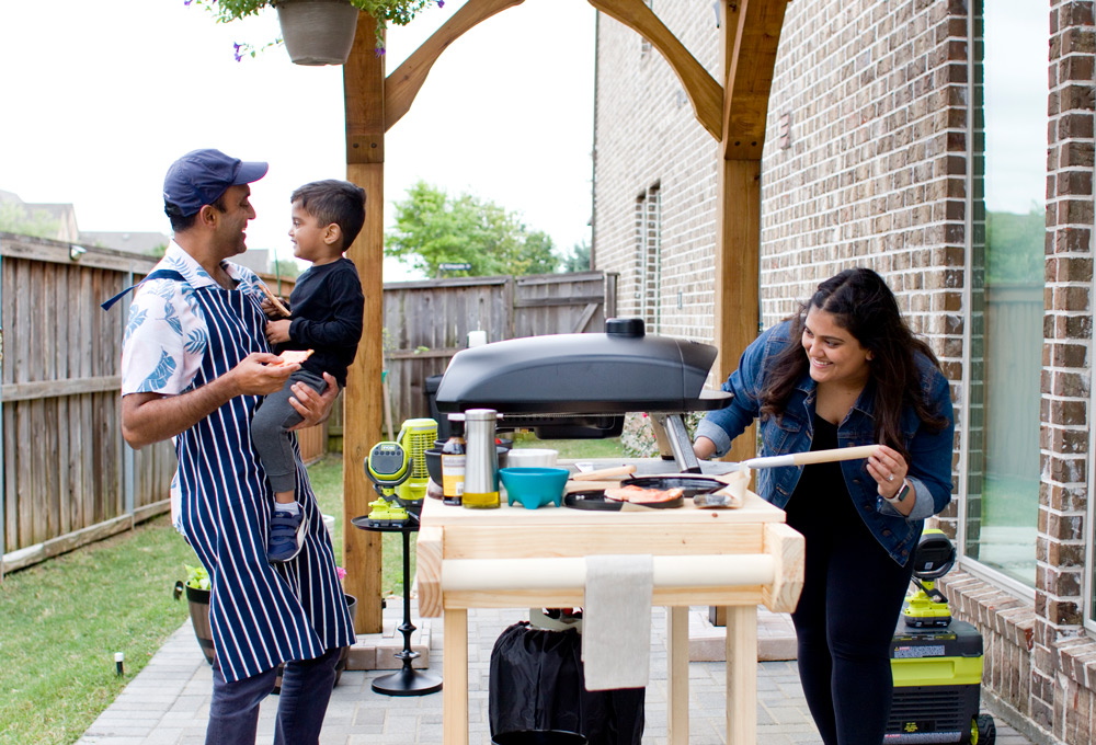 A man holding a child while a woman looks inside of a pizza oven.