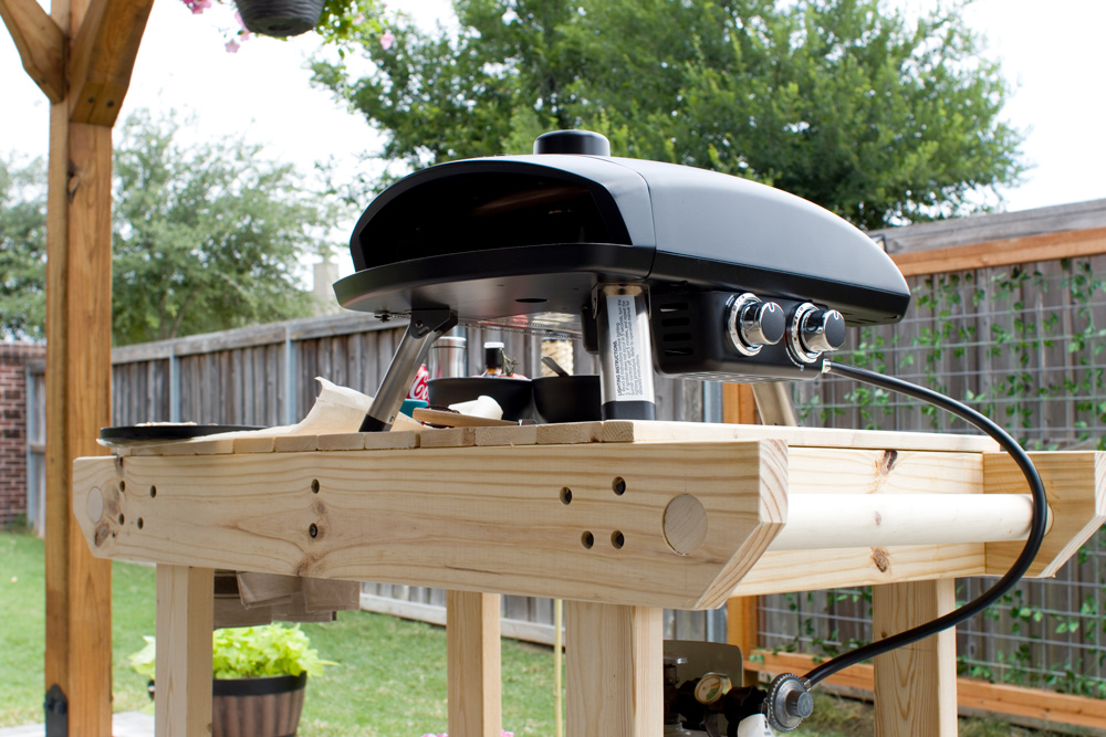 Close up of a pizza oven on top of a rolling wooden cart.