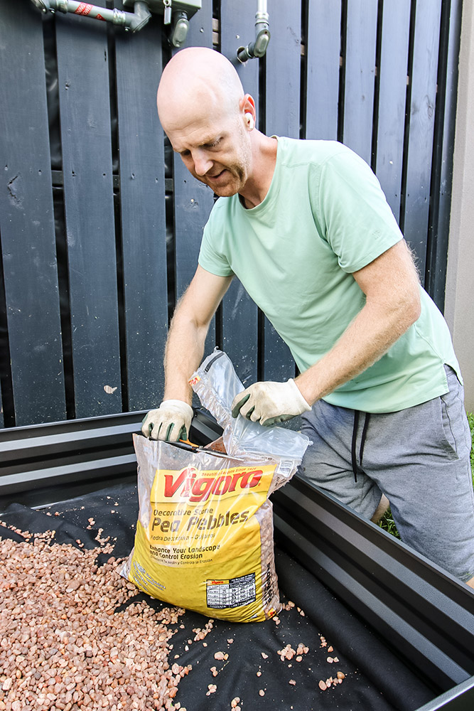 A man opening a package of vigoro pebbles and placing them in a raised flower bed.