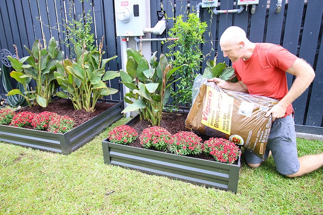 A man pouring a lair of brown mulch on the garden bed.