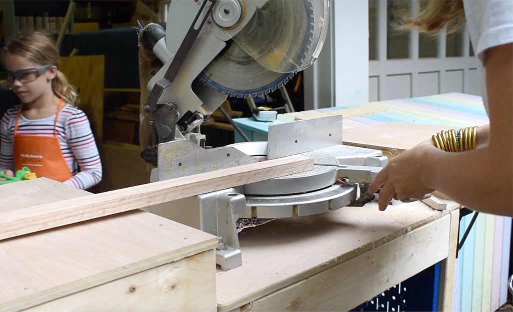 A person uses a miter saw to cut lumber. 