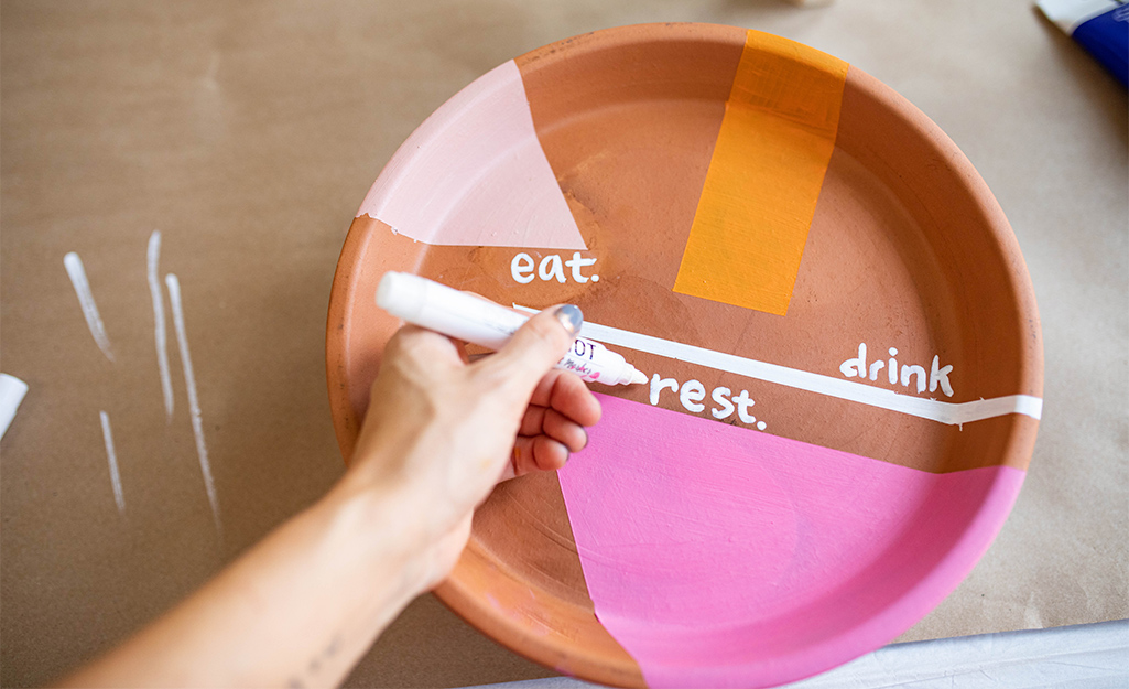 A person paints a pottery plate with words and colors. A person paints a pottery plate with words and colors.