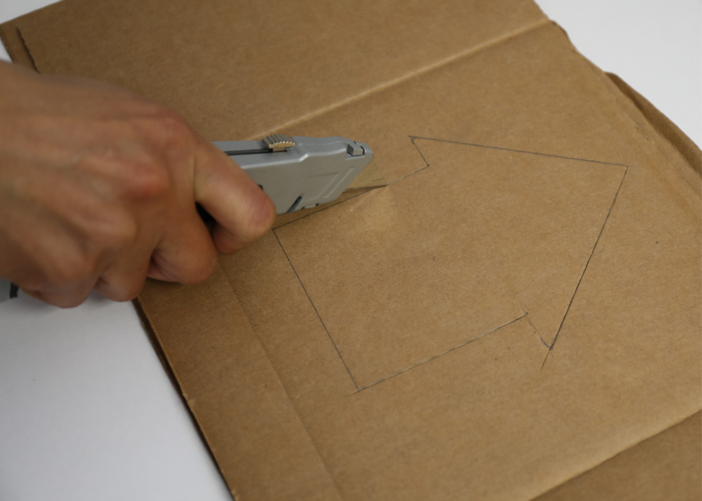 Shot of person cutting shape of house through cardboard