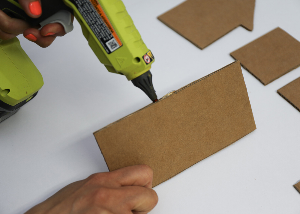 Shot of person applying hot glue to the edge of cardboard piece