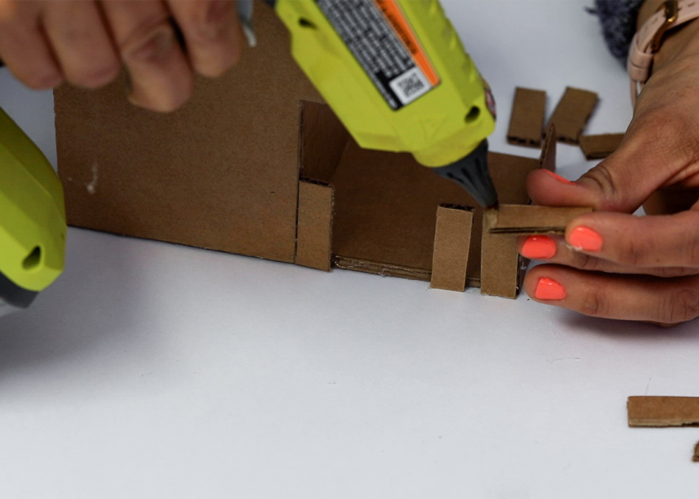 Shot of person applying hot glue to the edge of cardboard piece