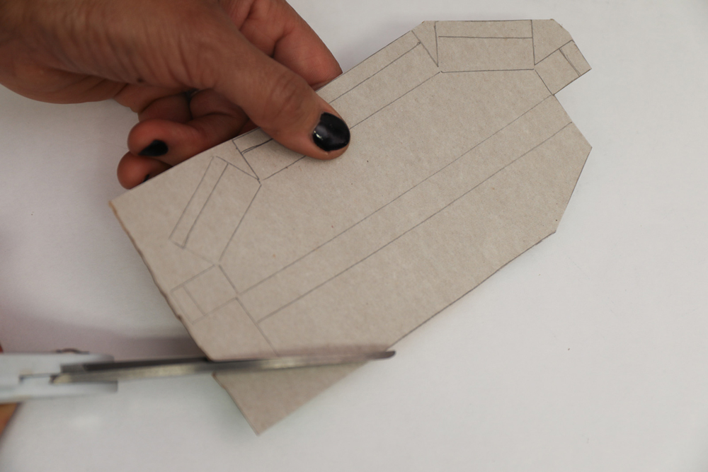 a hand holding cardboard with template lines drawn while scissors cut along lines