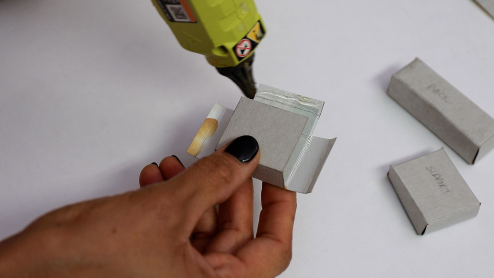 hand holding folded cardboard piece while hot glueing a tab piece