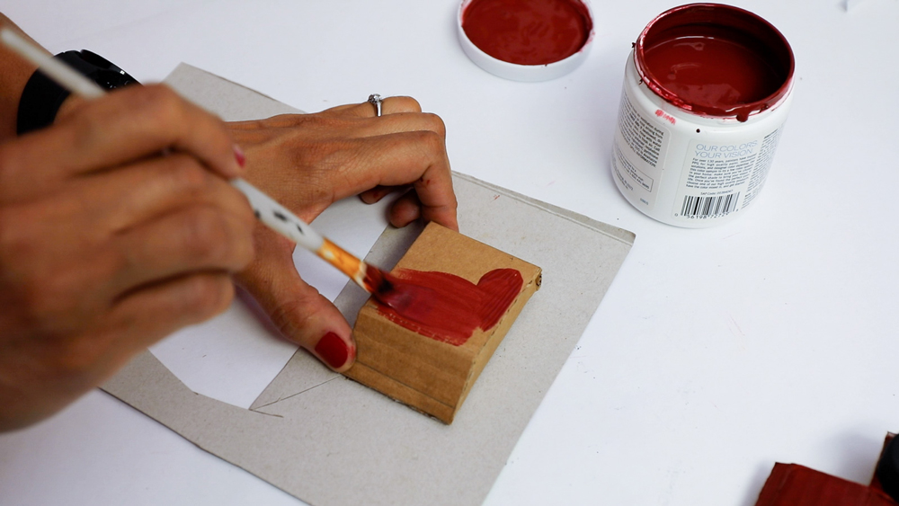 A woman’s hands painting a piece of folded cardboard red