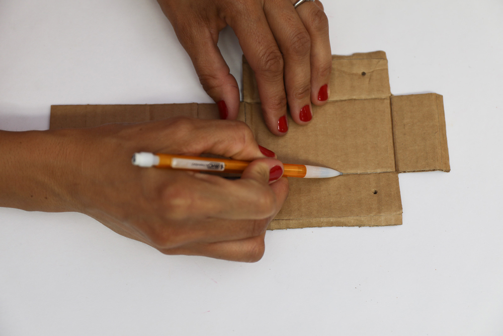 hands using a pencil to mark cardboard