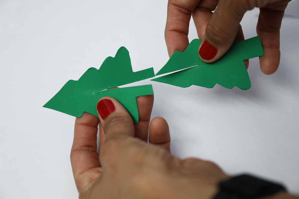 a woman’s hands assembling a green paper tree