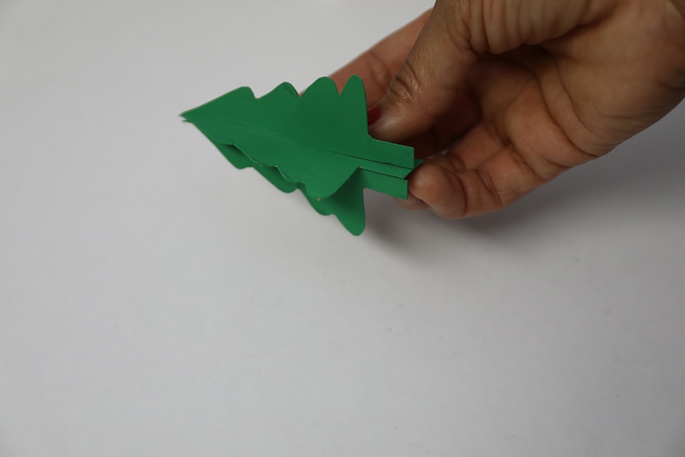 a hand holding an assembled green paper tree