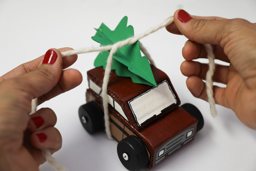 a woman’s hands tying yarn around a completed cardboard Christmas car