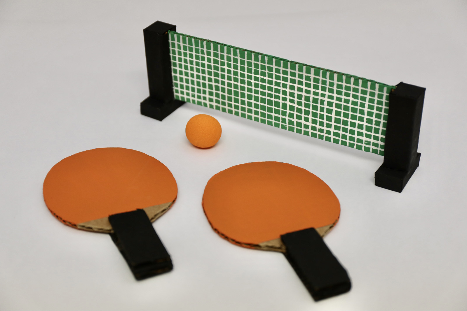 Two orange paddles, one small orange ball, and a green painted DIY tennis net