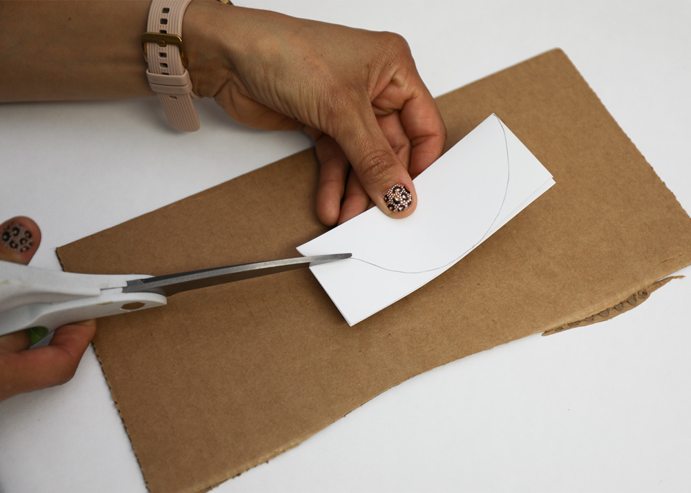 A hand cutting out a white piece of paper with scissors 