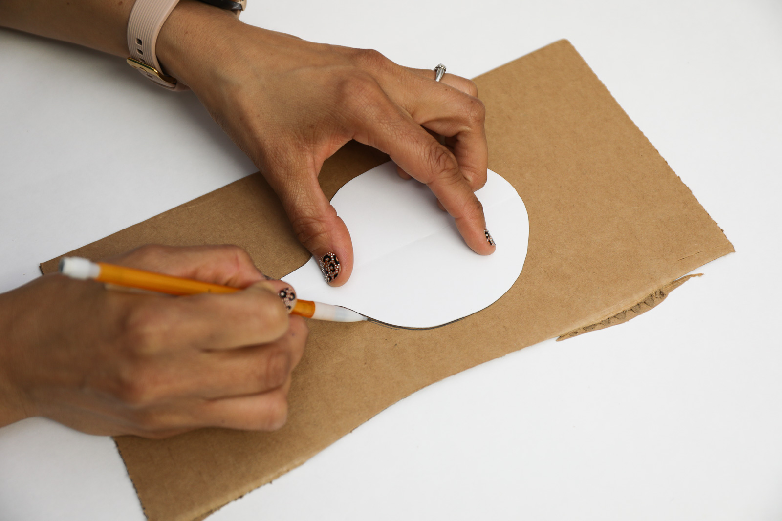 A person tracing a white paper cut out onto a piece of cardboard