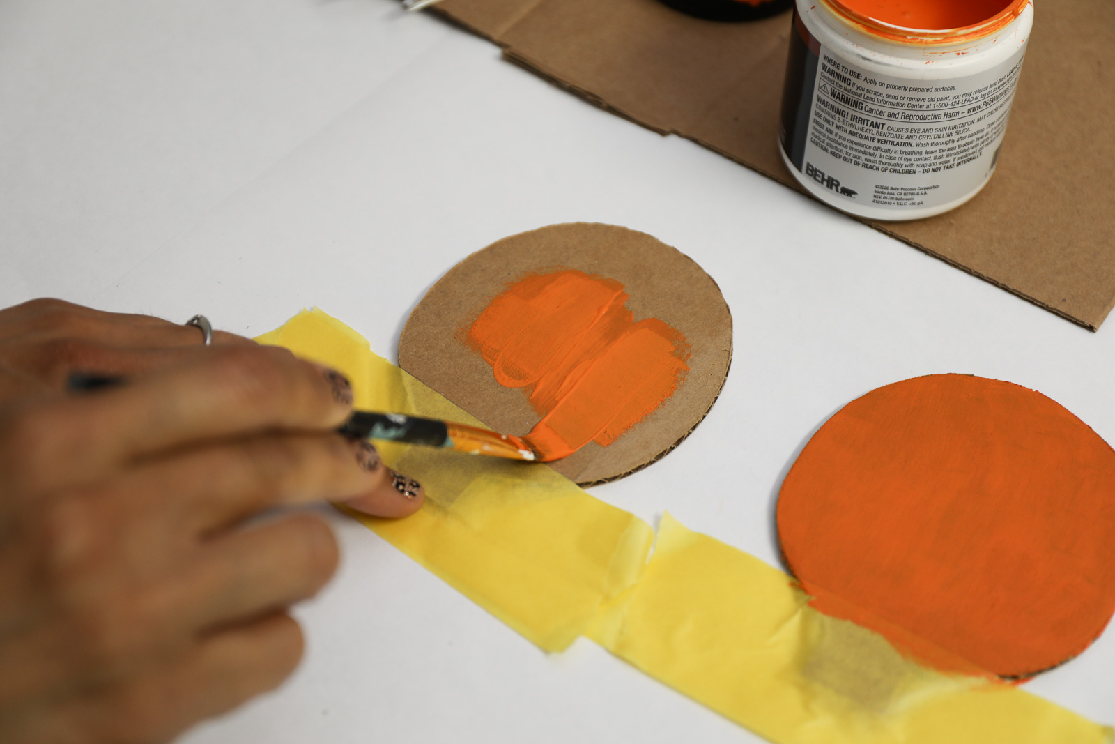 A person painting a circular piece of cardboard with orange paint