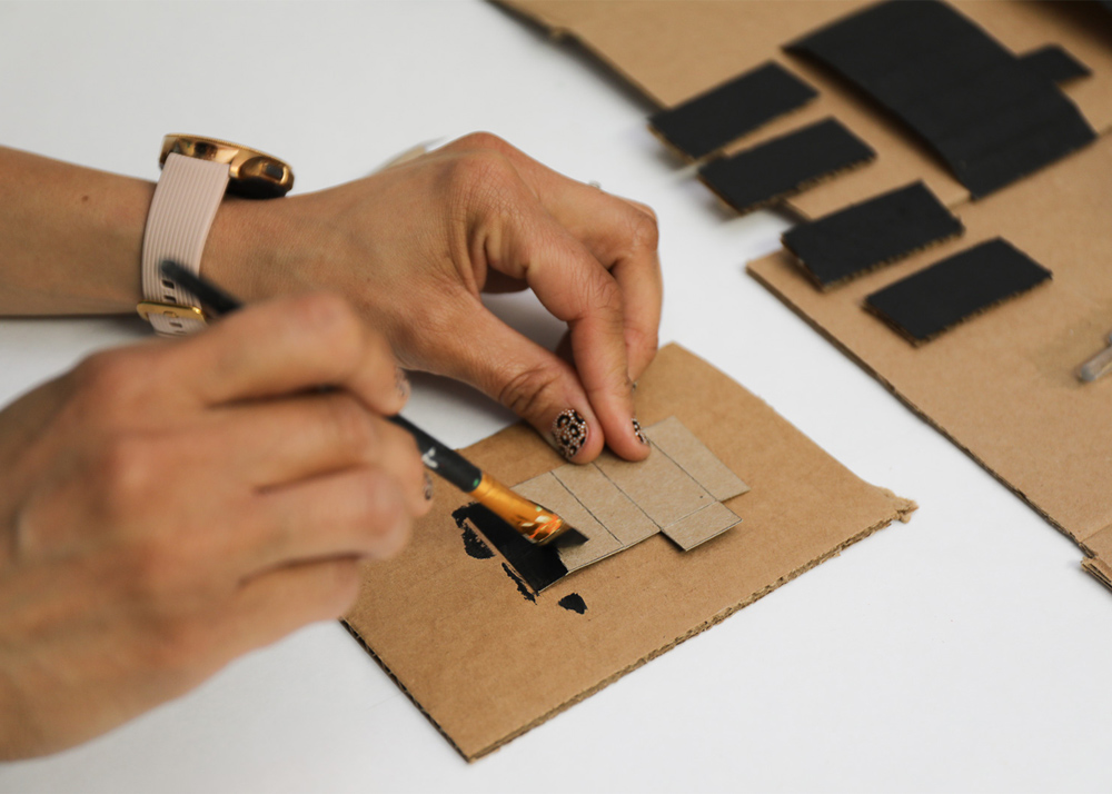 A person painting a piece of cardboard black 