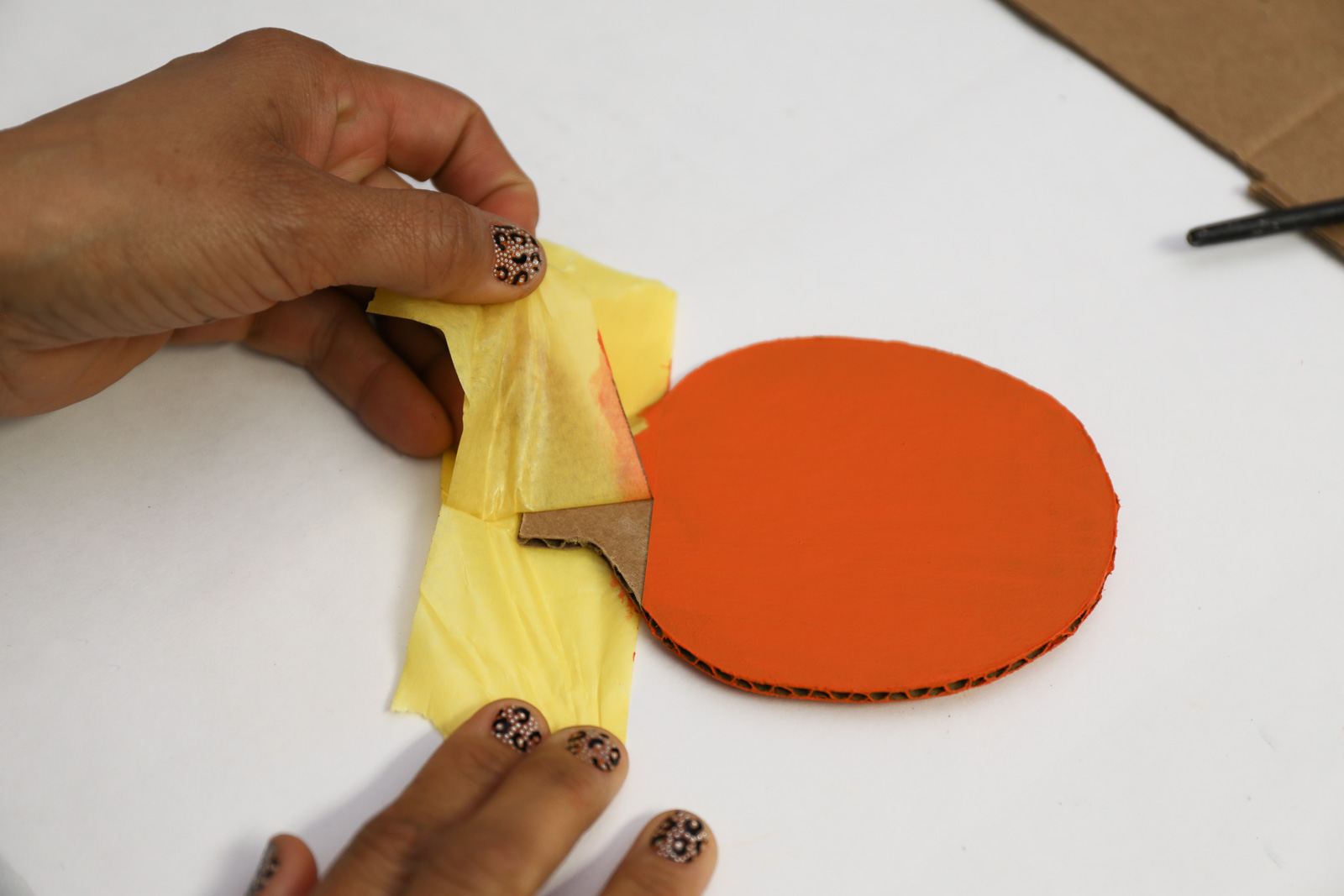 A person removing a piece of yellow tape from an orange painted cardboard cut out 