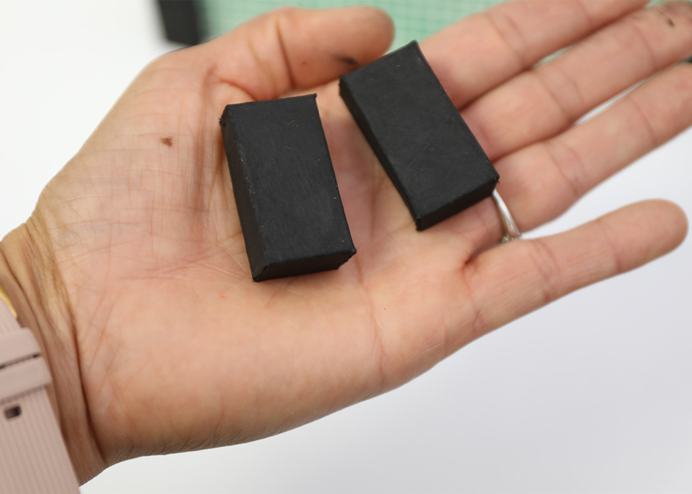 Two black painted rectangular boxes placed in a person’s hand