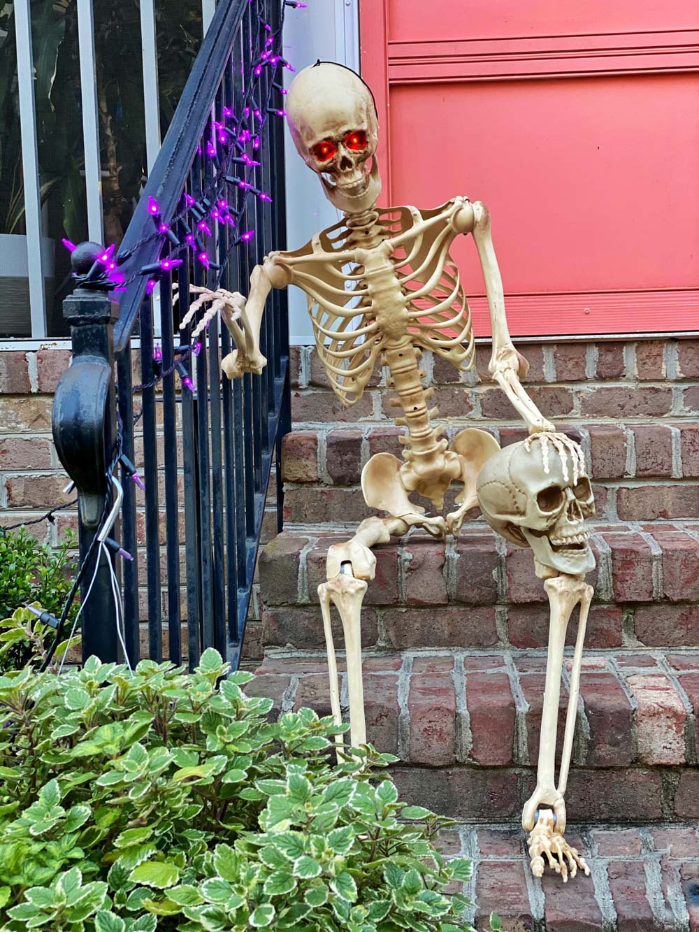 A skeleton sitting on brick steps with a skeleton head propped on its knee.