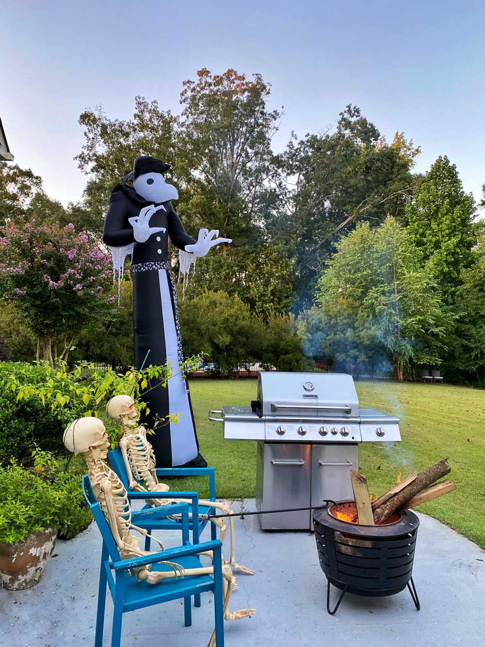 A giant black and white Victorian reaper standing over a pair of skeletons sitting at a fire pit.